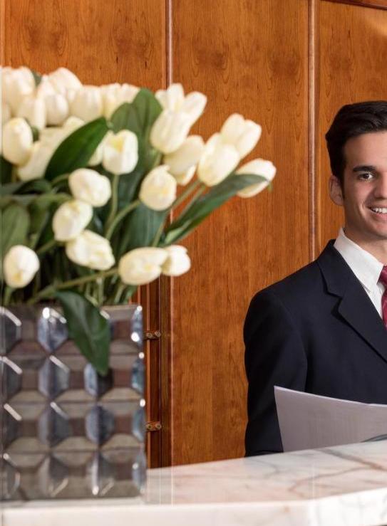 Arreglo floral de tulipanes blancos en un jarrón elegante en la recepción de una oficina, con un recepcionista sonriendo al fondo. Parte del servicio de ornamentación floral de Las Flores de la Reina