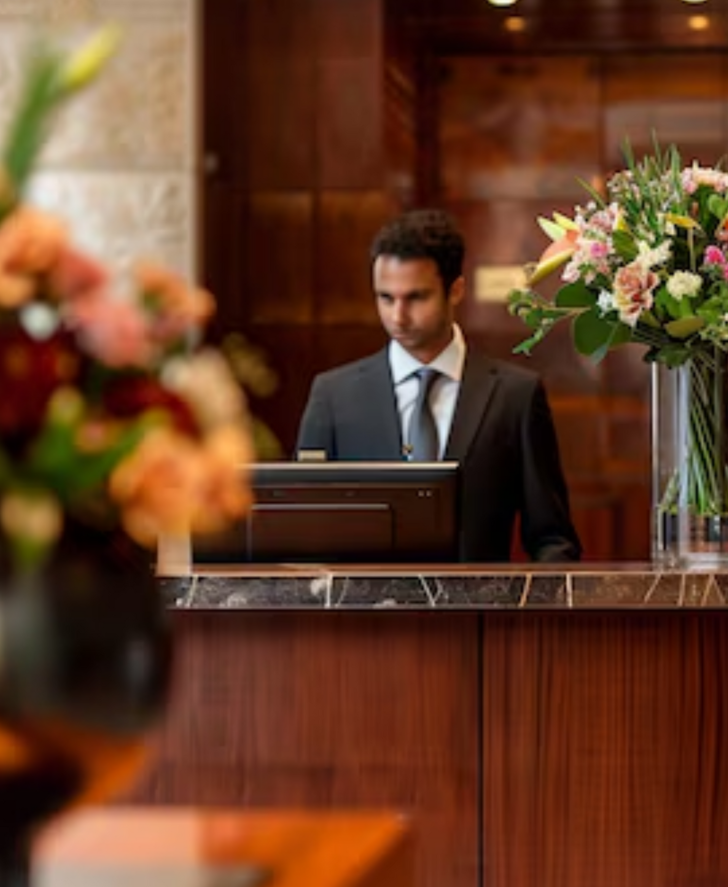 Arreglo floral en una recepción de oficina, parte del servicio de ornamentación de Las Flores de la Reina, con flores de colores cálidos y un recepcionista al fondo